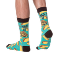 Lifestyle photo showing the 'You Had Me at Tacos' socks on a person's feet. The teal and yellow sock pattern is visible.