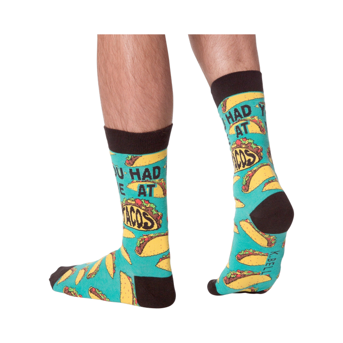Lifestyle photo showing the 'You Had Me at Tacos' socks on a person's feet. The teal and yellow sock pattern is visible.