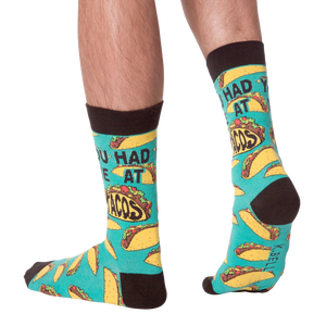 A pair of green socks with brown toes and heels. The socks have a pattern of tacos on them and the words 
