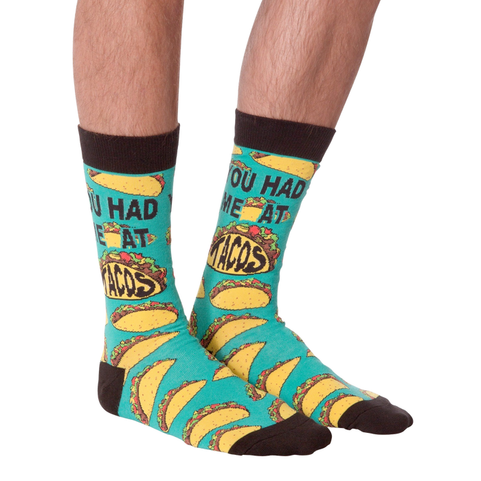 A pair of green socks with brown toes and heels. The socks have a pattern of tacos on them and the words 
