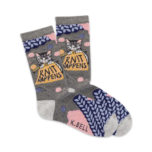 A pair of grey crew socks with a cute cat knitting a ball of yarn. The socks feature pink and blue knit accents and the phrase 'Knit Happens'.