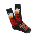 A pair of crew socks showcasing silhouetted climbers ascending a mountain against a vibrant sunset backdrop. The socks are mainly dark grey, red, and orange.