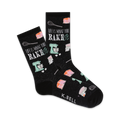 A pair of black crew socks with a baking-themed design. The socks feature pastel-colored images of cakes, whisks, and stand mixers, along with the text 'Life is what you bake it'.