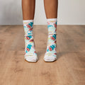 Lifestyle shot: Model's legs wearing Tropical Floral socks with white heels on a wood floor. [lf]
