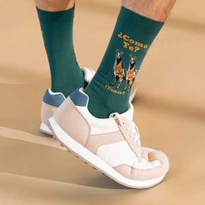 Lifestyle shot of a person wearing the green llama socks with beige sneakers on sand-colored surface.