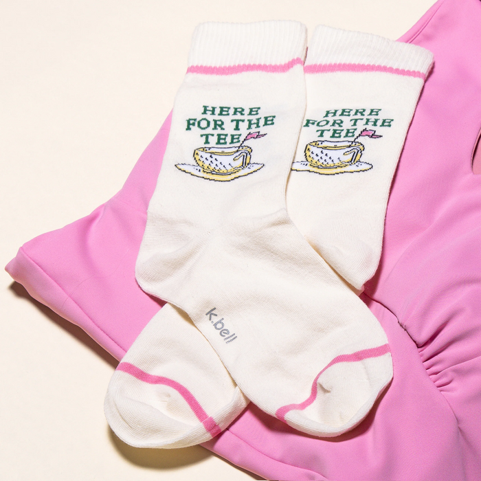 Lifestyle product shot of a pair of 'Here For The Tee' socks laying on a pink surface.