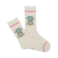 Pair of cream-colored crew socks with a pink cuff and embroidered golf-themed design: a golf ball resting in a teacup with the text 'Here For The Tee'.