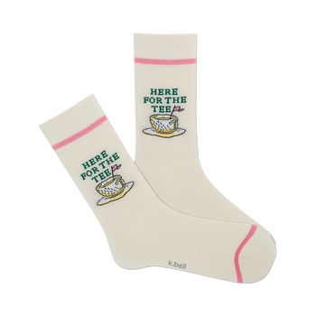 front view of a pair of white socks with pink and green designs of a teacup with a golf ball inside and the words 'here for the tee'.