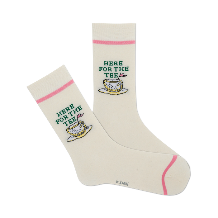 front view of a pair of white socks with pink and green designs of a teacup with a golf ball inside and the words 'here for the tee'.