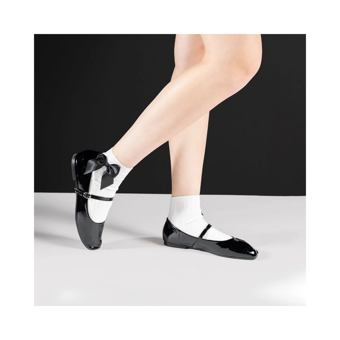 Lifestyle shot of a person wearing white ankle socks with a black bow and black patent leather shoes.