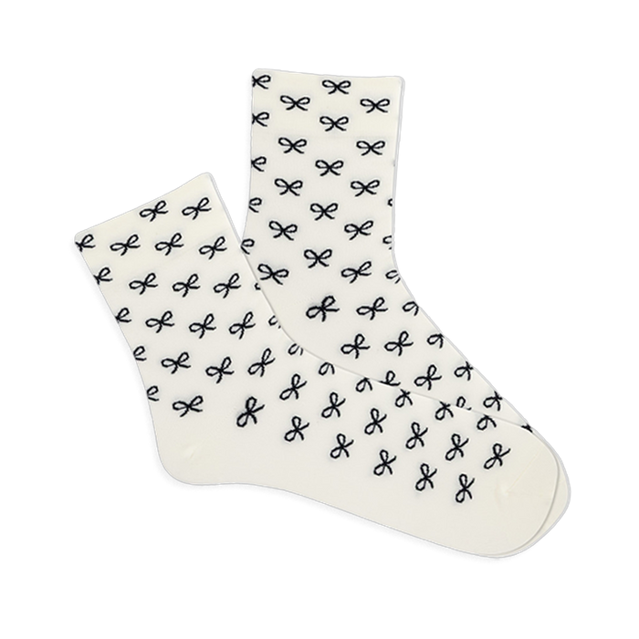 Pair of white microfiber anklet socks covered in a repeating pattern of small black bows, shown against a plain background. }}