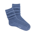 Pair of ribbed, slouchy crew socks in a dusty blue color, shown on a black background. 'k.bell' logo visible on sole.