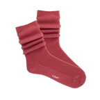 Pair of ribbed, slouchy crew socks in a muted red-orange color, shown on a black background. 'k.bell' logo visible on sole.