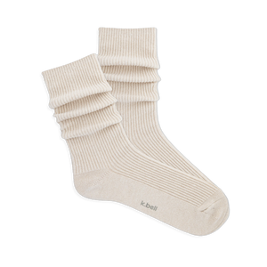 Pair of ribbed, slouchy crew socks in an off-white or cream color, shown on a black background. 'k.bell' logo visible on sole.
