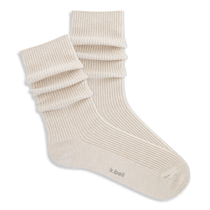 Pair of ribbed, slouchy crew socks in an off-white or cream color, shown on a black background. 'k.bell' logo visible on sole.