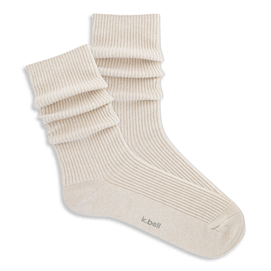 Pair of ribbed, slouchy crew socks in an off-white or cream color, shown on a black background. 'k.bell' logo visible on sole.