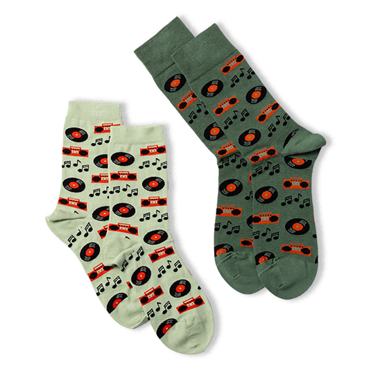 Two pairs of crew socks laid flat. One pair is light green with music patterns, the other is dark green with the same design.
