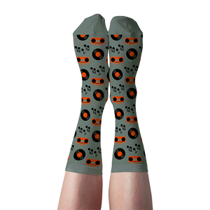 Person's legs wearing light green crew socks patterned with orange boomboxes, black records, and musical notes.
