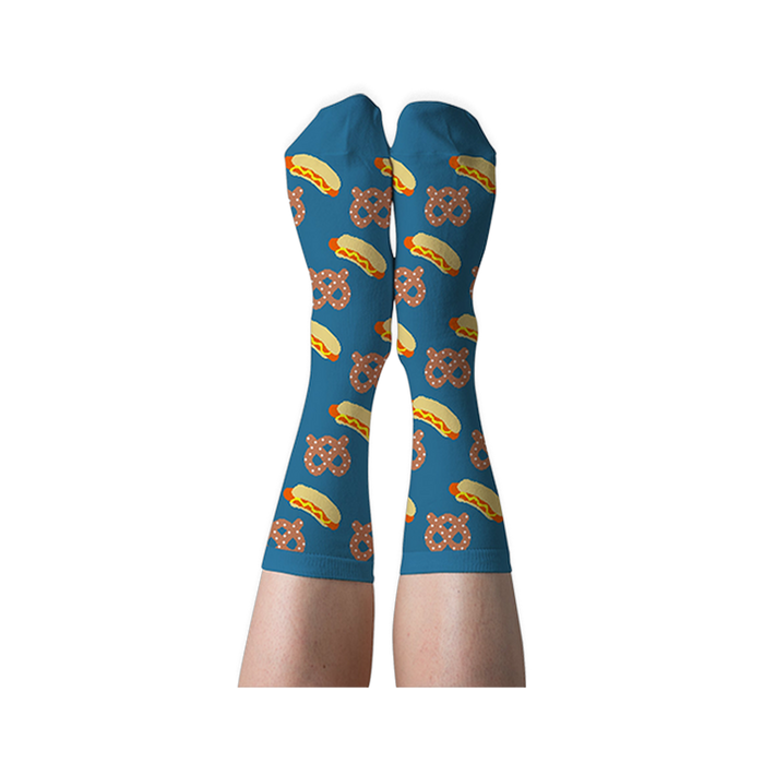 A person's legs wearing blue crew socks with hot dog and pretzel pattern, shown with soles facing up against a dark background.