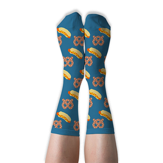 A person's legs wearing blue crew socks with hot dog and pretzel pattern, shown with soles facing up against a dark background.