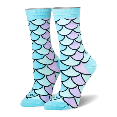 Crew socks featuring a mermaid scale pattern in pastel blue, teal, and lilac with black outlines and solid light blue cuffs.