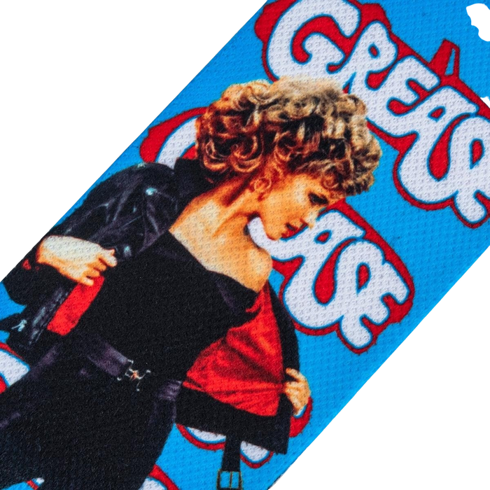 A blue background with a partial image of Sandy from the movie Grease. She is wearing a black jacket and red shirt. The word 