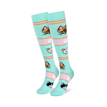 Mint green tall socks on foot models showing orange, brown, and tuxedo cat faces with pink striped bands and paw prints.