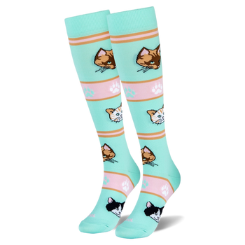 Mint green tall socks on foot models showing orange, brown, and tuxedo cat faces with pink striped bands and paw prints.