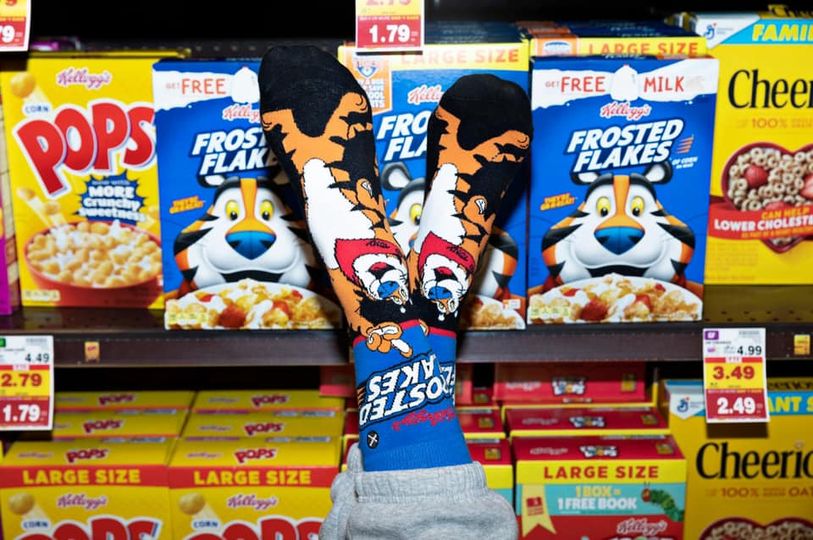 Lifestyle photo: Person wearing Frosted Flakes socks with cereal boxes in the background. [lf]