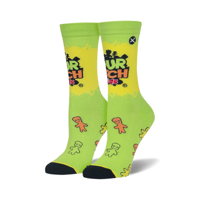 A pair of crew socks, lime green and yellow, with the Sour Patch Kids logo and scattered candy figures. Black toes and heels.