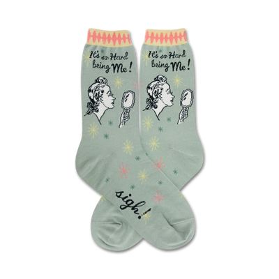 green crew socks with an illustration of a woman looking in a mirror and saying it's hard being me.  the text sigh can be seen on the foot