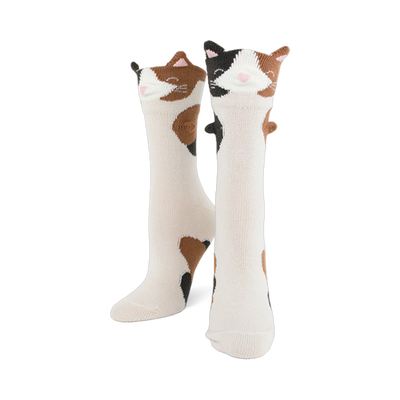 Pair of creamy white crew socks featuring calico cat faces with 3D ears and brown and black patches down the leg.
