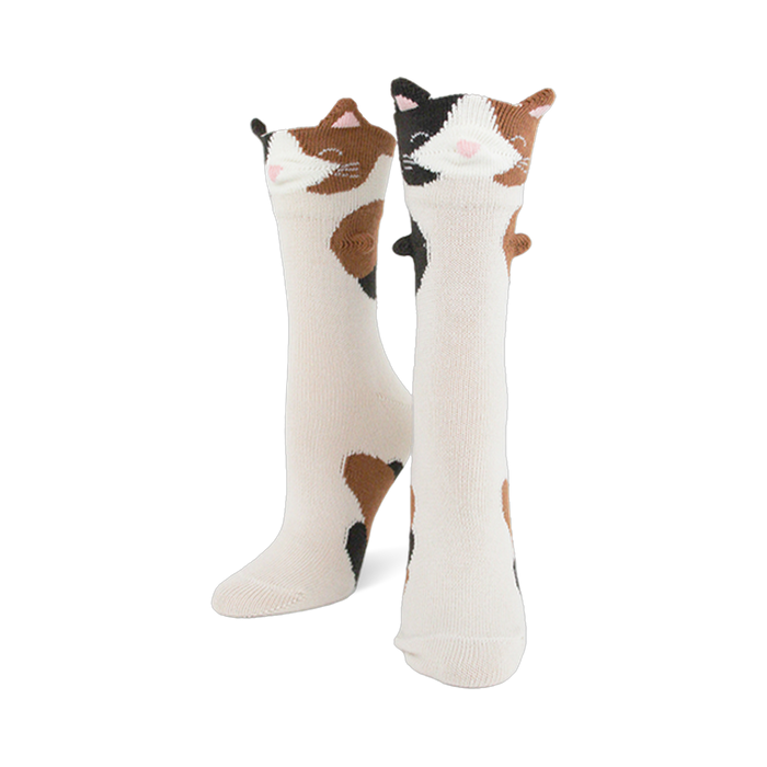 Pair of creamy white crew socks featuring calico cat faces with 3D ears and brown and black patches down the leg. }}