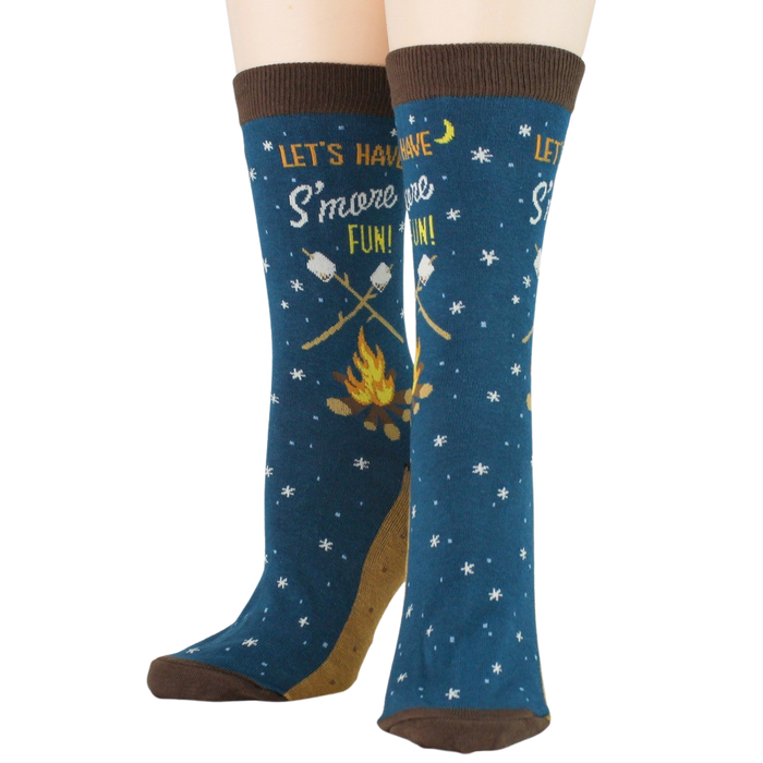 A pair of blue socks with a brown toe, heel, and cuff. The socks have a pattern of white stars and brown sticks with marshmallows roasting over a campfire. The words 