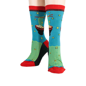 A pair of blue socks with a pattern of chopsticks holding noodles over a bowl of ramen. The socks have a red toe, heel, and cuff.