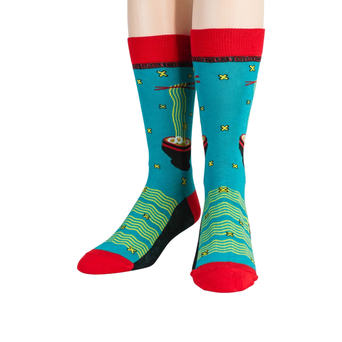 A pair of blue socks with a pattern of red chopsticks and black bowls of ramen noodles on a green background. The socks have a red top and a black heel and toe.