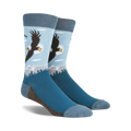 A pair of blue crew socks with a graphic design of a bald eagle soaring over a mountain landscape. 