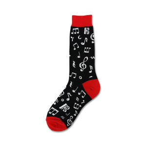 A pair of black socks with red toes and musical notes printed all over. The socks are laying on top of open sheet music with a red background. There is a silver triangle and a red and white harmonica also laying on the sheet music. The piano keys are visible underneath the sheet music.