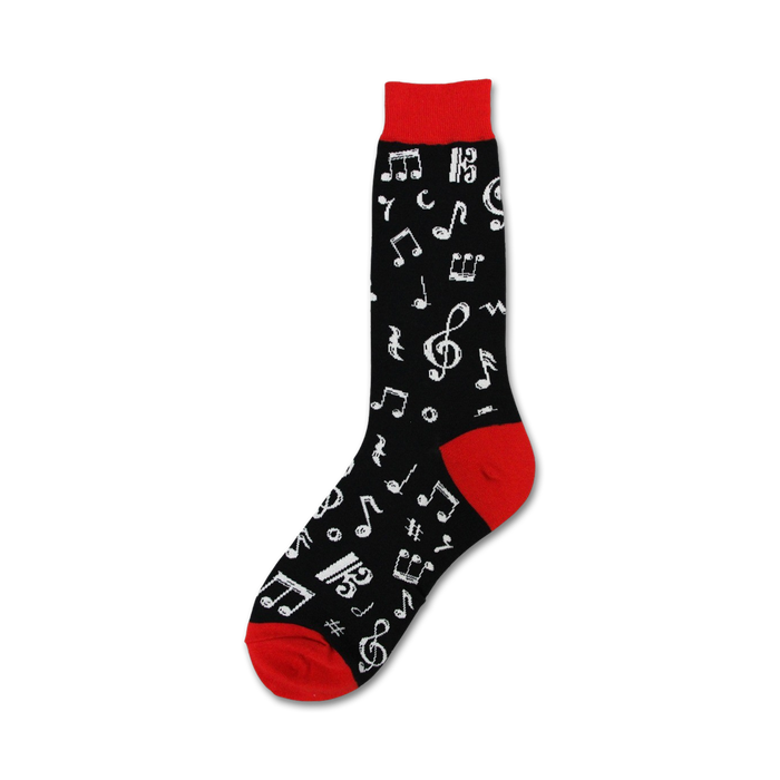 A pair of black socks with red toes and musical notes printed all over. The socks are laying on top of open sheet music with a red background. There is a silver triangle and a red and white harmonica also laying on the sheet music. The piano keys are visible underneath the sheet music.