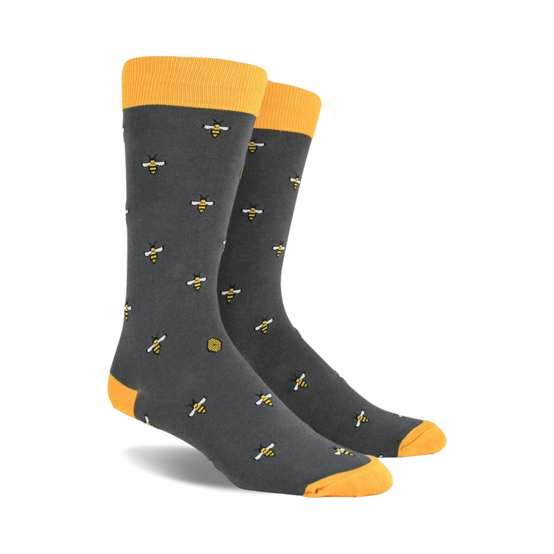 A pair of charcoal gray crew socks with a repeating pattern of yellow bees and honeycombs. Yellow tops.