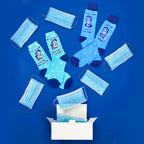 Flat lay product shot of two pairs of 'Mask' socks with several light blue disposable masks and a white box on a blue background. [lf]