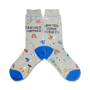 gray crew socks with blue toes, heels, and cuffs. pattern of multicolored crafting supplies, including scissors, tape measures, yarn, and buttons. text "crafiness is happiness" and "crafters gonna craft" knit into socks. womens.   