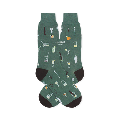 Green crew socks patterned with small bar tools, mixed drinks, and the text cocktail snob. Features dark heels and toes.