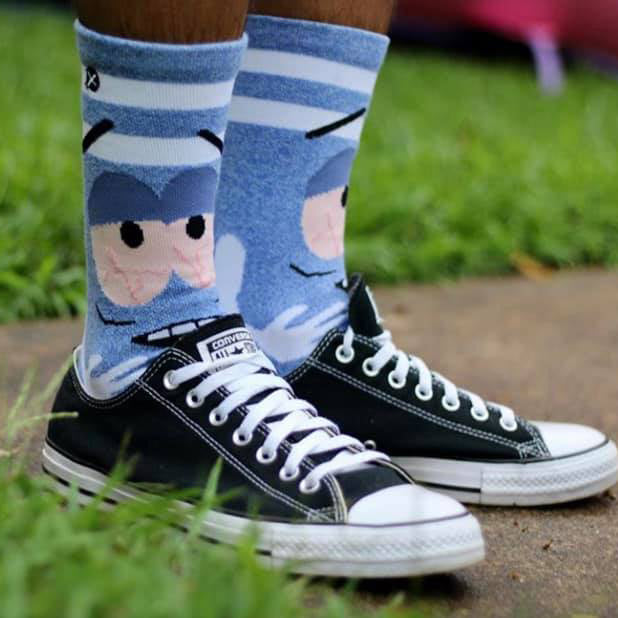 A pair of blue socks with a cartoon character from South Park on them. The socks are worn with a pair of black Converse sneakers.