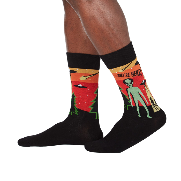 Lifestyle shot of a person wearing the 'They're Here' alien socks. Shows how the socks look when worn.