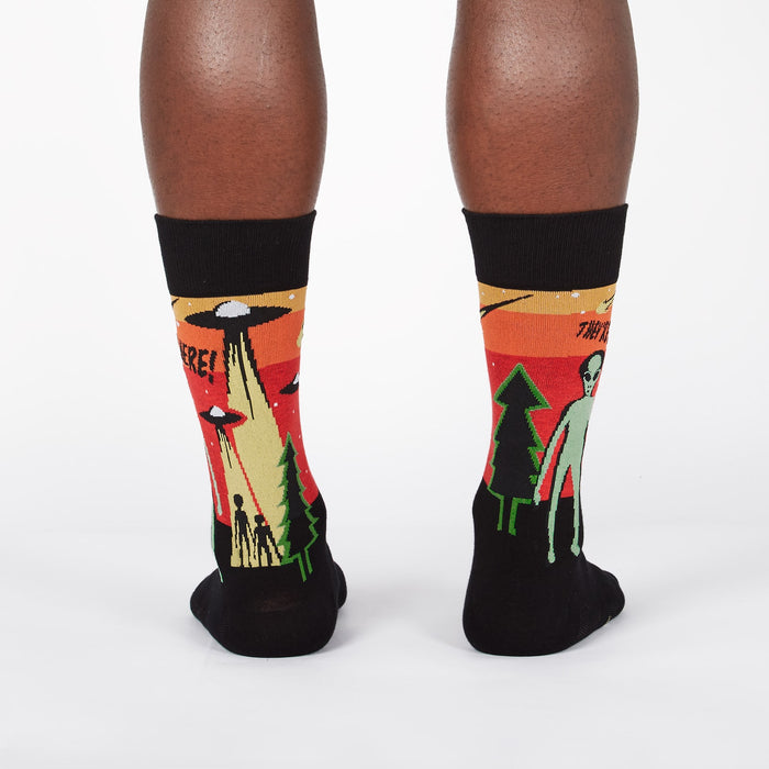 A pair of black socks with a colorful pattern of a UFO beaming up a human and an alien standing next to a tree. The text on the socks says 