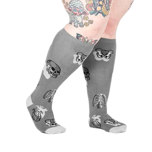 Lifestyle shot showing a model wearing the anatomical knee-high socks.  The socks are gray with skulls, ribcages, and hearts.