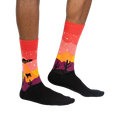 Lifestyle shot of a person wearing the Area 51 crew socks. Socks are red, orange, and purple with a desert scene featuring a UFO and cacti.