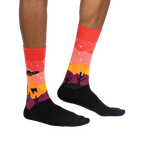 Lifestyle shot of a person wearing the Area 51 crew socks. Socks are red, orange, and purple with a desert scene featuring a UFO and cacti.
