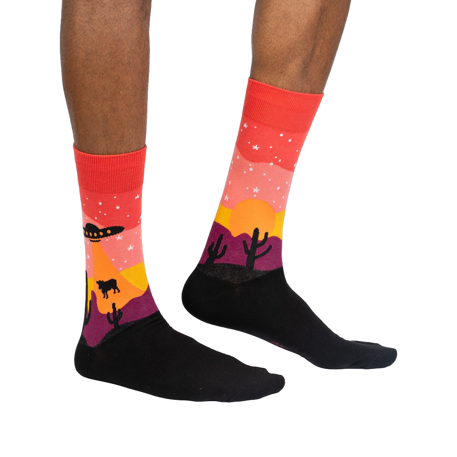 Lifestyle shot of a person wearing the Area 51 crew socks. Socks are red, orange, and purple with a desert scene featuring a UFO and cacti.